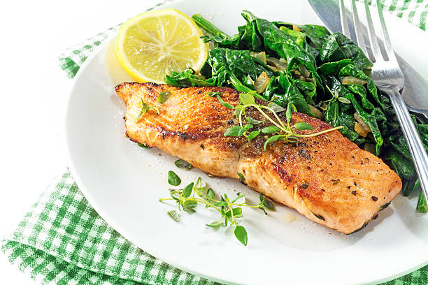 grilled salmon with thyme, lemon and spinach on a plate, vegetarian low carb dish, green white napkin on a white background, selected focus, narrow depth of field